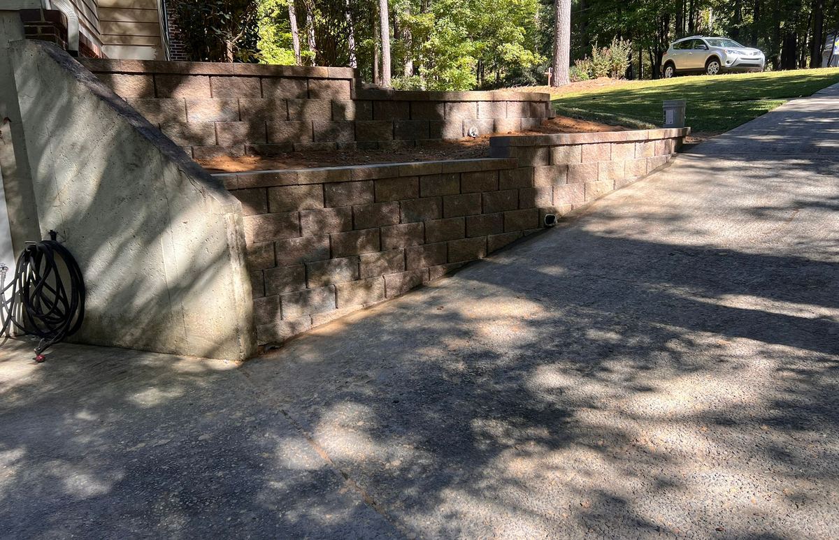 Block retaining wall built by EM Landscape & Hardscape Design alongside a driveway